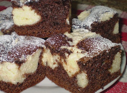 Az összekevert kakaós piskótára túrós krémet szaggatott. Csodás Boci szeletet vett ki a sütőből