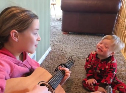 A kislány két éves Donw szindrómás öccsét tanítja beszélni úgy hogy együtt énekelnek